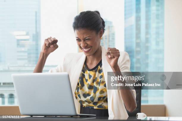 mixed race businesswoman cheering at laptop at office desk - super computer stock-fotos und bilder