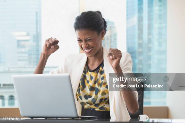 mixed race businesswoman cheering at laptop at office desk - business people cheering in office stockfoto's en -beelden