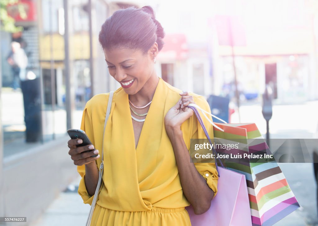 Mixed race woman texting on cell phone holding shopping bags