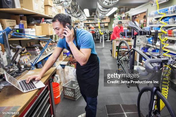technician using cell phone and laptop in bicycle repair shop - shopping with bike stock-fotos und bilder