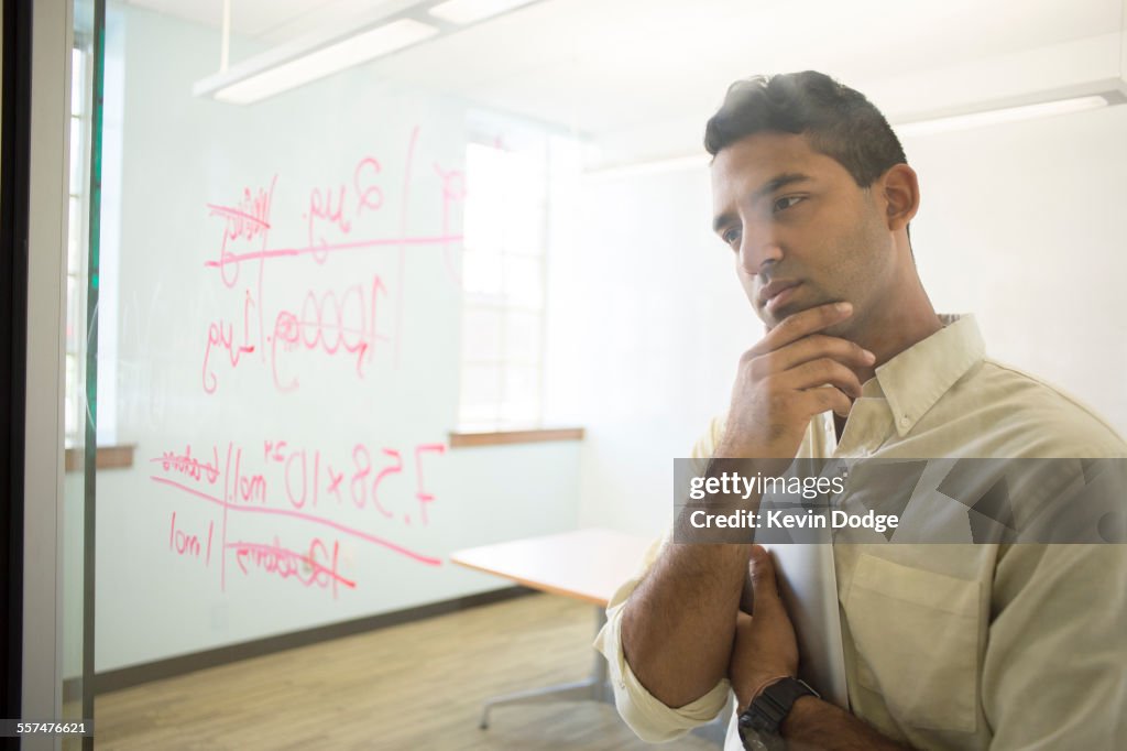Asian businessman examining writing on glass window in office