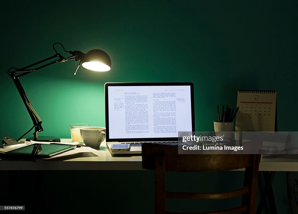 Computer and cell phone illuminated by desk lamp at night