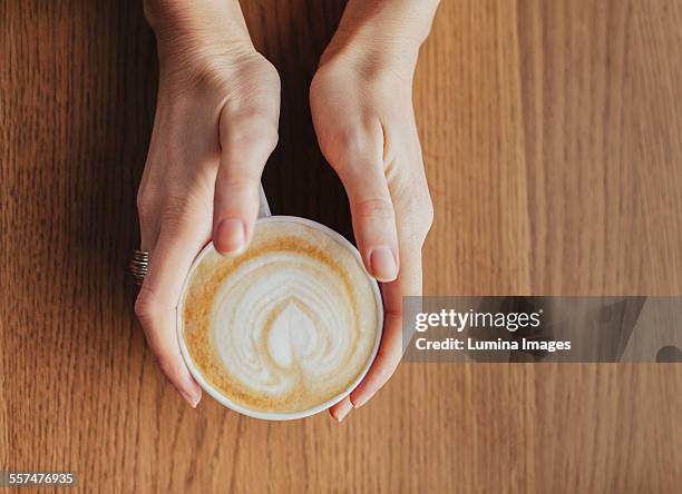 hands holding cup of coffee with leaf drawn in milk - tazza di latte dall'alto foto e immagini stock