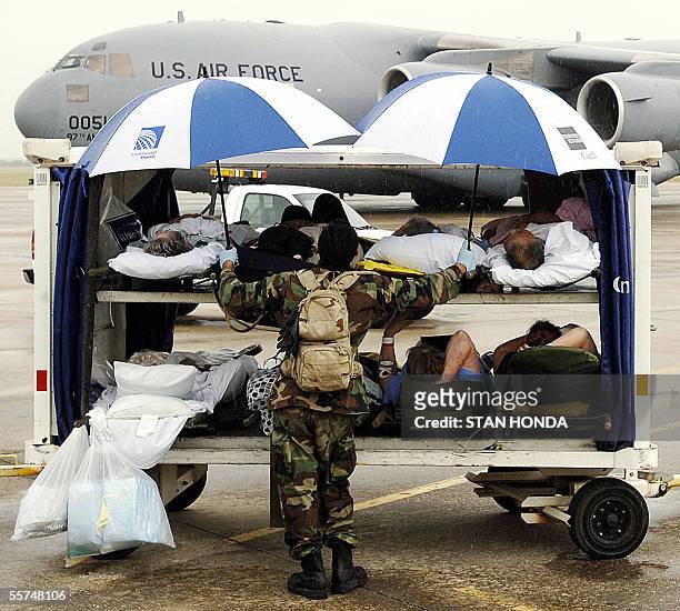 National Guard soldier protects elderly patients on a luggage cart with umbrellas before they are transported to a waiting C-17 cargo plane , 23...