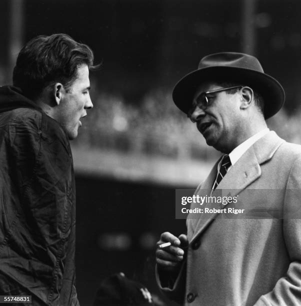 American professional football coach Vince Lombardi holds a lit cigarette and talks to professional football player Frank Gifford of the New York...