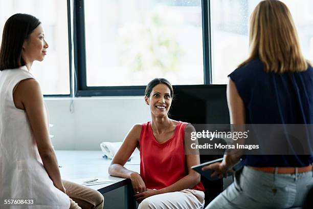 businesswoman discussing with colleagues at desk - red tops stock pictures, royalty-free photos & images