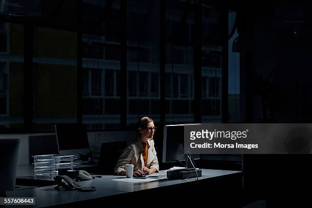 geschäftsfrau mit computer im dunklen büro - dunkel stock-fotos und bilder