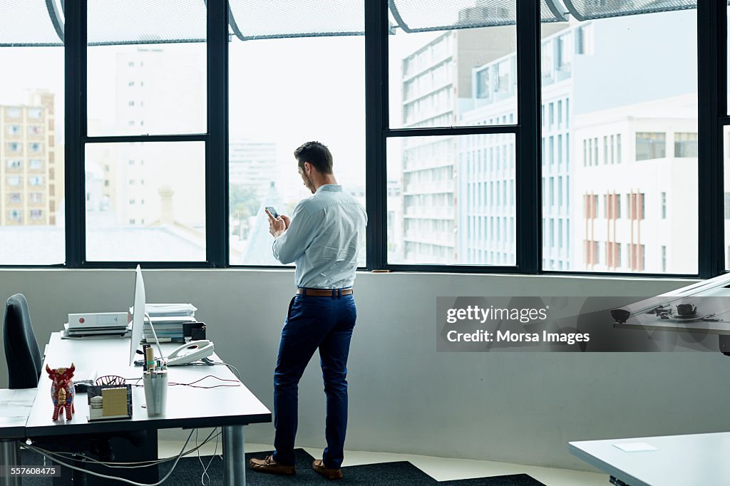 Businessman using mobile phone by office window