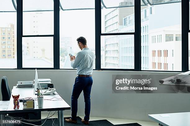 businessman using mobile phone by office window - blue shirt back stock pictures, royalty-free photos & images