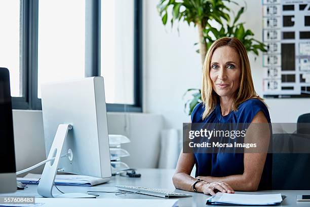 confident mature businesswoman sitting at desk - bright blue eyes stock pictures, royalty-free photos & images