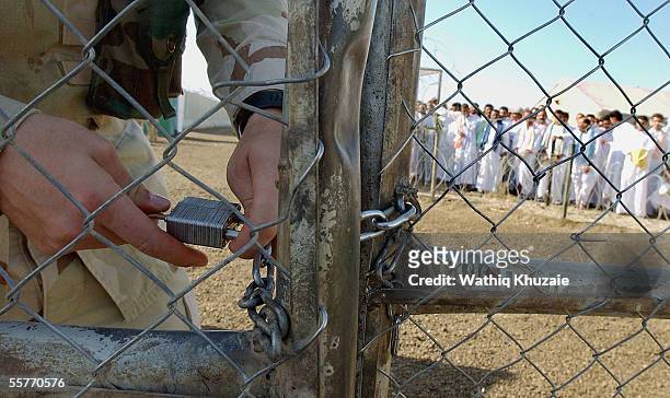 Soldier unlocks a gate as Iraqi detainees stand in line to be processed for release from Abu Ghraib prison facility on September 26, 2005 in Abu...
