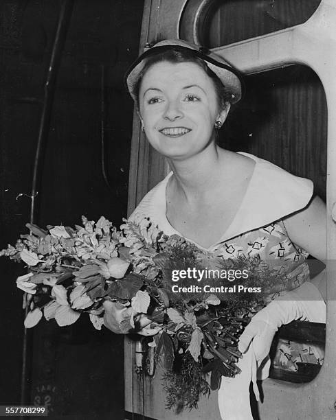 Actress Jane Wenham holding a bouquet of flowers and leaning out of a train carriage, as she and the rest of the Old Vic Theatre Company prepare to...