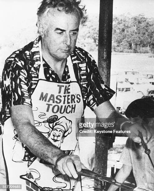Australian Prime Minister Gough Whitlam wearing a comical apron as he cooks outdoors on a barbecue, circa 1975.