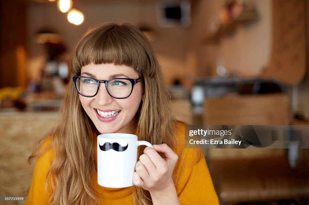 Girl smiles drinking out of moustache mug