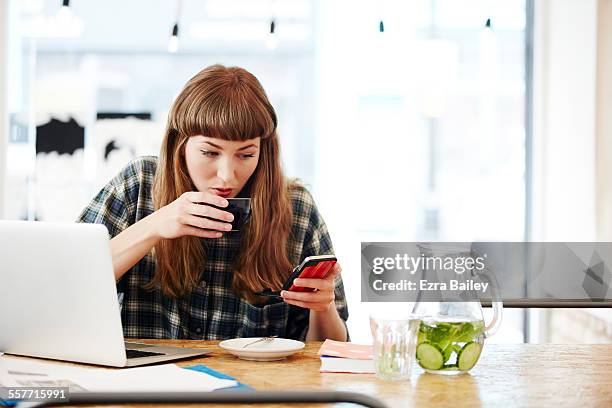 girl drinking coffee checking her phone - mobile device on table stock pictures, royalty-free photos & images