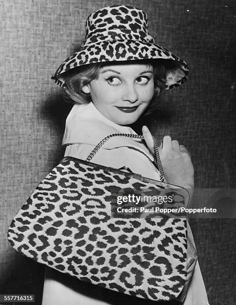 English actress Jill Ireland wearing a leopard print hat and carrying a matching handbag as she attends a fashion show in London, circa 1960.