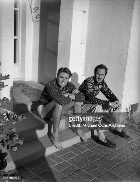 Actor Peter Lawford and actor Keenan Wynn pose on the steps of a house in Los Angeles, California.