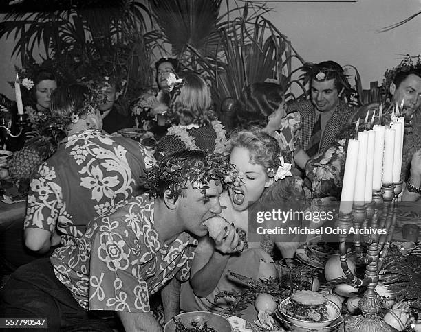 Actor Jackie Coogan is fed by his wife actress Betty Grable as Ken Murray looks on during a party in Los Angeles, California.