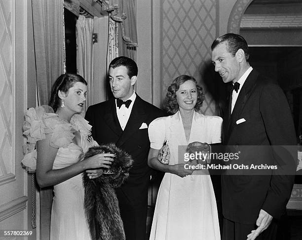 Actor Robert Taylor talks with Veronica Cooper as actress Barbara Stanwyck talks with actor Gary Cooper during an event in Los Angeles, California.