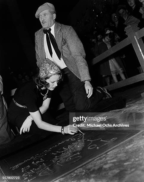 Actress Eleanor Powell signs her name in cement in front of Grauman's Chinese Theatre with the help of Jean W. Klossner in Los Angeles, California.