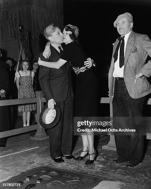 Actress Eleanor Powell hugs Sid Grauman of Grauman's Chinese Theatre after having her hand and foot print ceremony with the help of Jean W. Klossner...