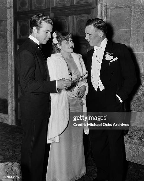 Actor Dick Powell with his wife actress Joan Blondell talk with actor Walter Huston during an event in Los Angeles, California.