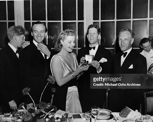 Singer Rudy Vallee presents a gift to Ann Sheridan with actors David Niven and Otto Kruger during an event in Los Angeles, California.