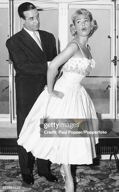 French filmmaker Christian-Jaque fixes the dress of his wife, actress Martine Carol , as she poses for pictures as they arrive in London, April 26th...