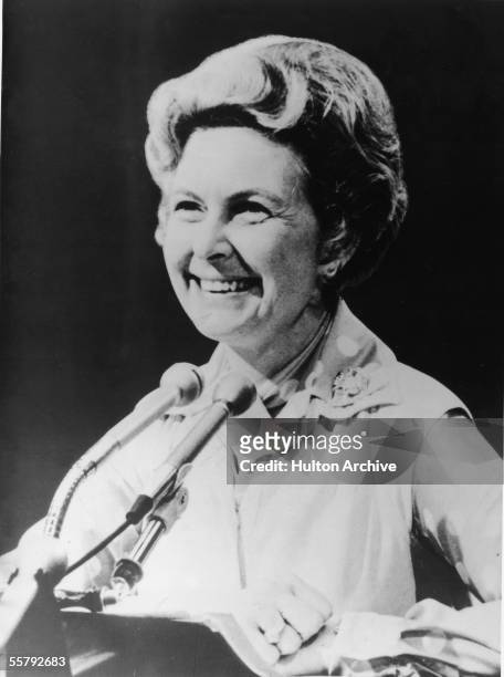 American political activist Phyllis Schlafly smiles from behind a pair of podium mounted microphones, 1982.
