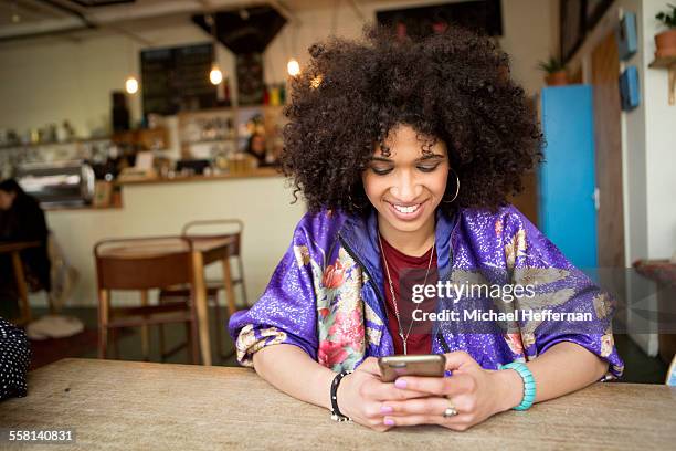 young woman smiles at phone in cafe - purple jacket stock pictures, royalty-free photos & images