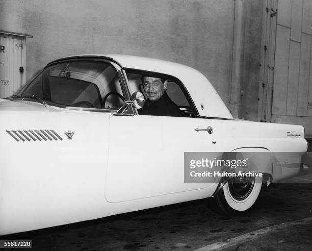American actor Clark Gable sits in his 1955 Ford Thunderbird sports car and smiles, late 1950s.
