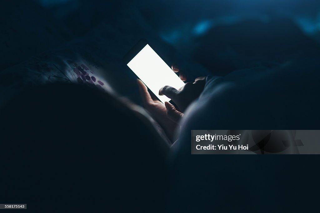 Woman texting and reading on smartphone in bed