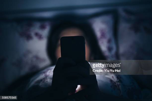 woman reading and texting on smartphone in bed - verslaving stockfoto's en -beelden
