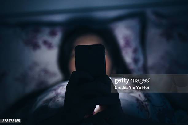 woman reading and texting on smartphone in bed - dependency stock pictures, royalty-free photos & images