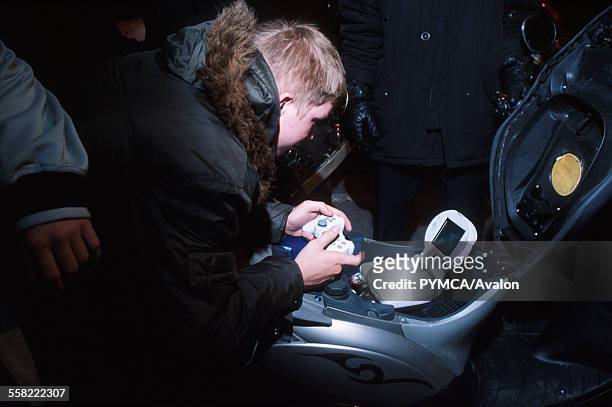 Teenage boy plays a playstation, installed on a scooter, Luton, UK 2004.