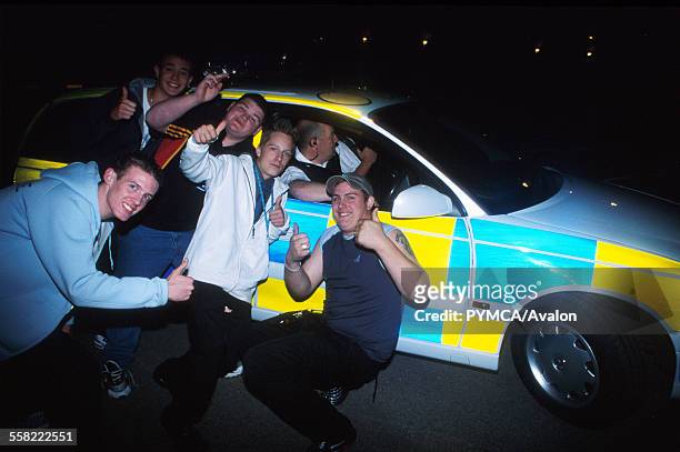 Group of teenagers smiling and posing next to a Police car, Luton, UK 2004.