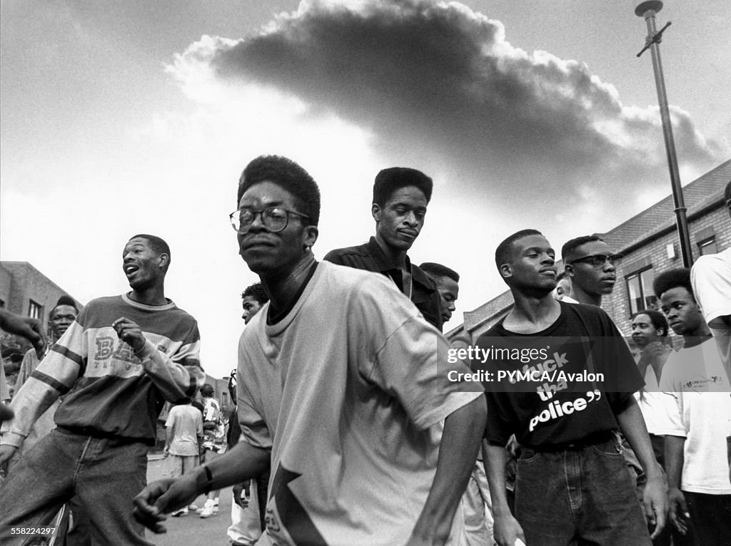 Men with flat top haircuts dancing in the street as an ominous storm cloud rolls overhead, Notting Hill Carnival, London, UK, 1990s