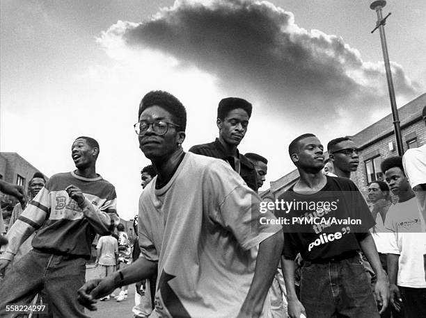 Men with flat top haircuts dancing in the street as an ominous storm cloud rolls overhead, Notting Hill Carnival, London, UK, 1980s.