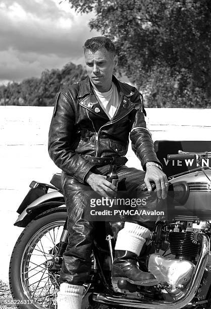 50s style Rocker sitting on a vintage motorbike, drinking beer..