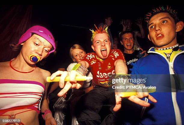 Ravers wear fluorescent clothing with dummy, glow-in-the-dark, spikey hair and glowsticks, Cream, Liverpool, 2000s.