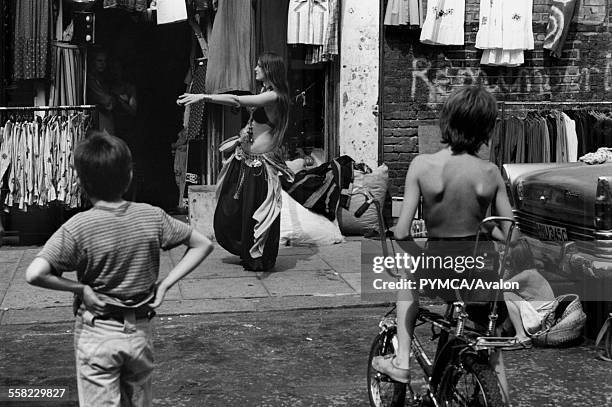 Two boys one on a Chopper watch a woman belly dancing Portobello Road market London August 1975.