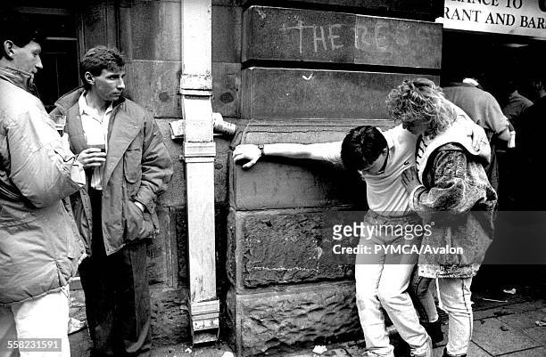 Woman supports drunken man as drinkers look on outside a pub in Cardiff on the day of the Rugby International 1989.