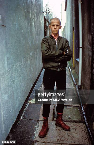 Kenny, a young skinhead standing in an alley way wearing cherry red Dr Marten boots, Brighton, UK 12th Feb 1983.