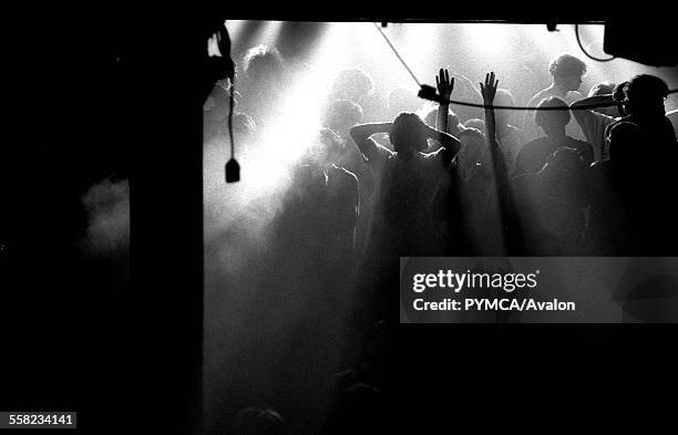 Clubber raises their hands on an atmospheric main stage during a break in the music at the Hacienda, Manchester 1988.