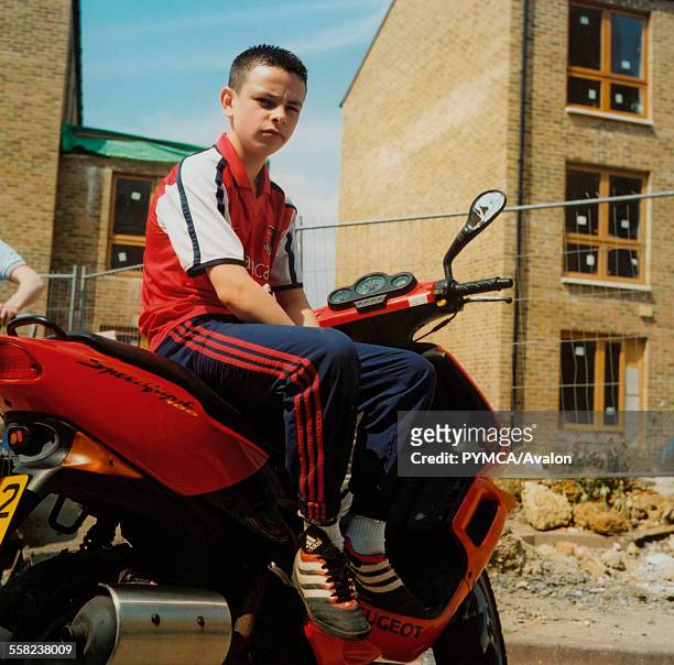 Boy sitting on a moped in a newly built housing complex.