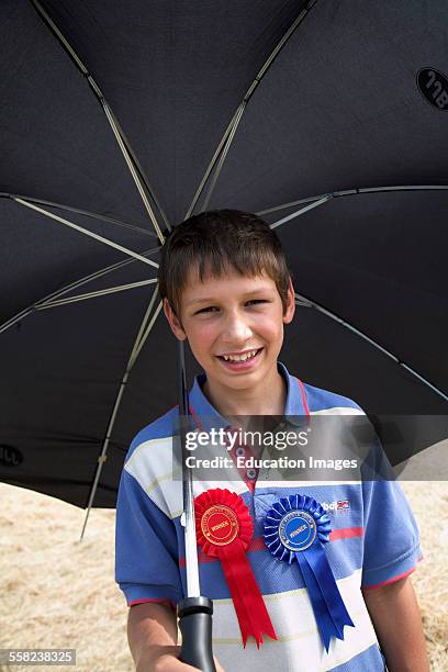 Red and blue winner badges on a boys chest as he holds a big black umbrella, Butley, Suffolk, England