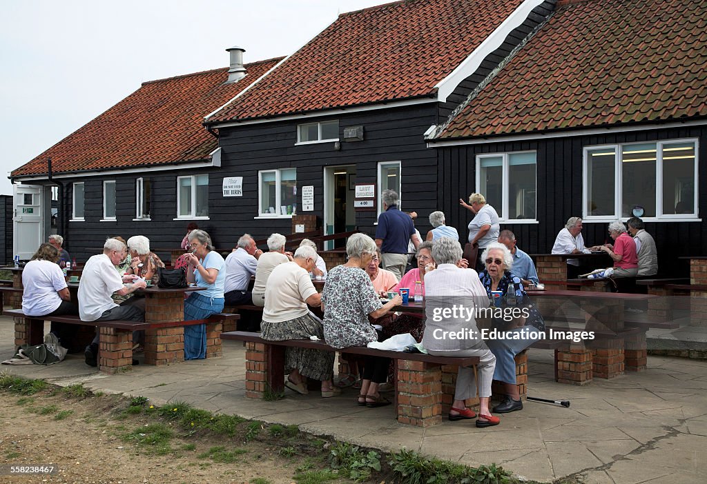 Elderly people eating outside eating fish and chips at the Flora tea rooms cafe, Dunwich, Suffolk, England,