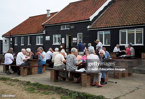 Elderly people eating outside eating fish and chips at the Flora tea rooms cafe, Dunwich, Suffolk, England,