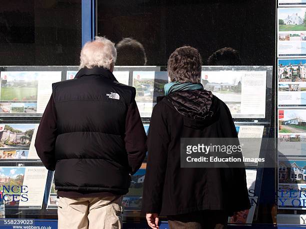 Old couple looking at houses in an estate agents window, Bude, Cornwall