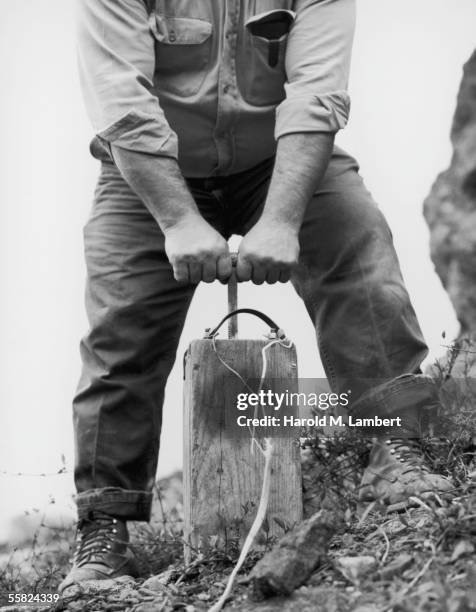 Workman prepares to press the plunger of a detonator, 1965.